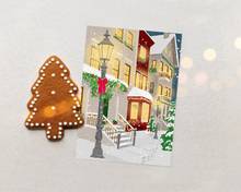 Lade das Bild in den Galerie-Viewer, Klassische Weihnachtskarte in einem Flatlay mit Weihnachtsdekoration. Die Karte zeigt eine elegante Illustration einer Kleinstadt in einer Winternacht mit weihnachtlichter Dekoration und Winterlichtern