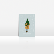 Lade das Bild in den Galerie-Viewer, Postkarte für deine Weihnachtsgrüße: Eine Frau trägt eine Tanne im Schneegestöber mit modernem Schriftzug wundervolle Weihnachten