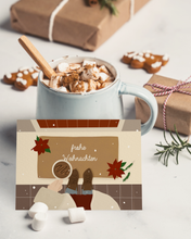Lade das Bild in den Galerie-Viewer, moderne Weihnachtskarte mit weihnachtlich dekoriertem Hauseingang und mit Spruch frohe Weihnachten auf einem Tisch mit heißer Schokolade