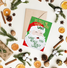 Lade das Bild in den Galerie-Viewer, Das Bild zeigt eine witzige Weihnachtskarte für die Generation Y mit Weihnachtsmann Illustration im Cartoon Stil und Spice Girls Songtext &quot;so tell me what you want what you really really want&quot; mit oassendem Kraftapier Briefumschlag in A6 in einem Flatlay mit festlicher Dekoration.
